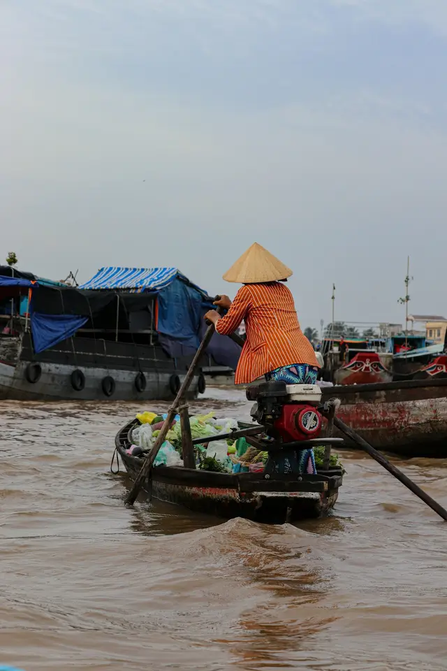 A woman in a conical hat rowing her boat at the floating market