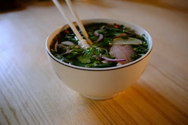 A steaming bowl of noodle soup with fresh herbs