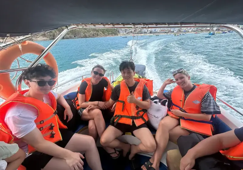 Four guests in life jackets on the boat crossing from Nhơn Lý, the village on the shore behind