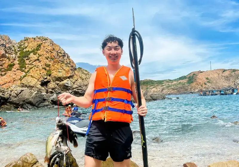 Guest in a life jacket on the pebble beach with a speargun and the morning catch