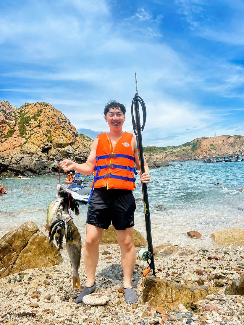 Guest in a life jacket on the pebble beach with a speargun and the morning catch