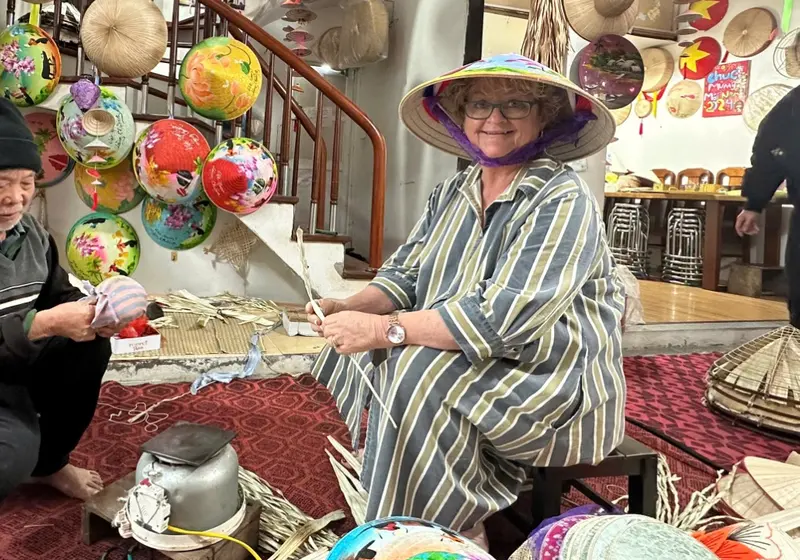 A guest wearing a freshly painted conical hat beside the artisan