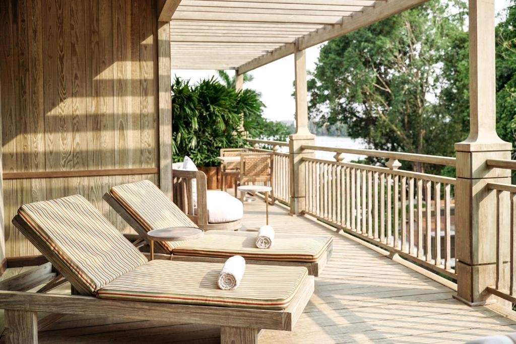 Two striped loungers with rolled towels on a covered timber balcony with white railings, trees and the Saigon River beyond