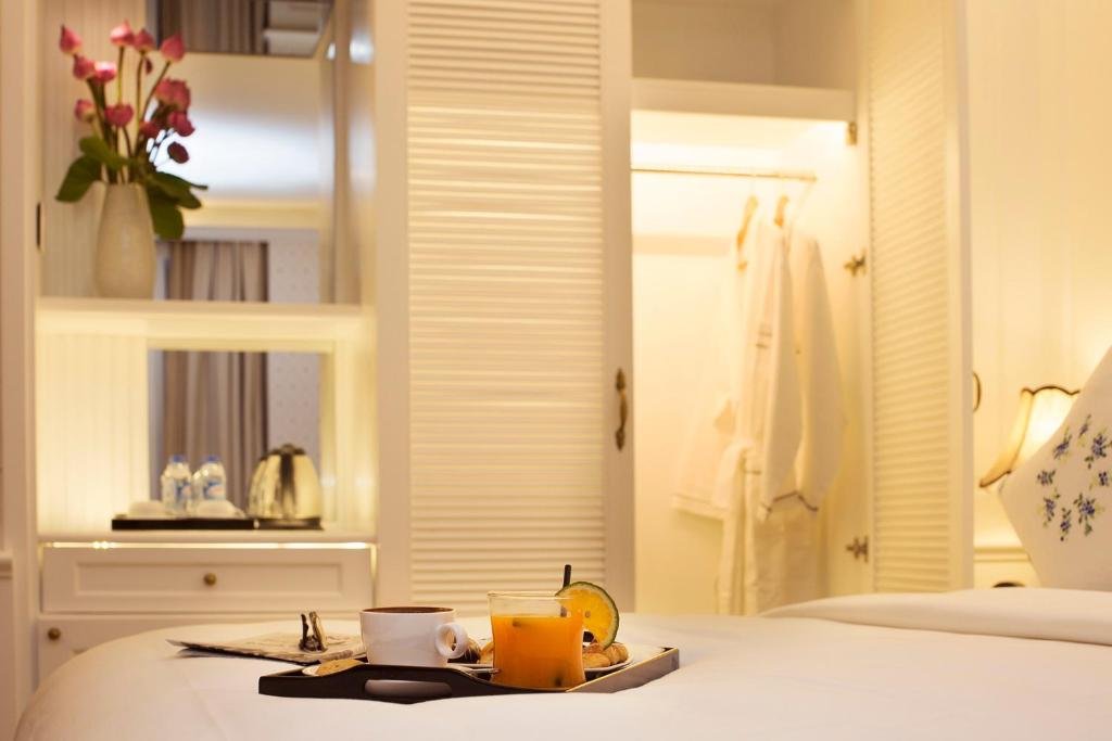 A breakfast tray with coffee and orange juice on the bed, the open wardrobe with bathrobes behind, and lotus flowers and a kettle on the shelves
