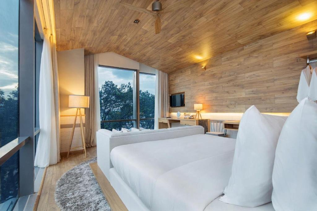 From the pillows: the sofa, a tripod lamp and the corner windows at dusk, a wall-mounted TV and a long desk on a timber wall, and bathrobes on a rail