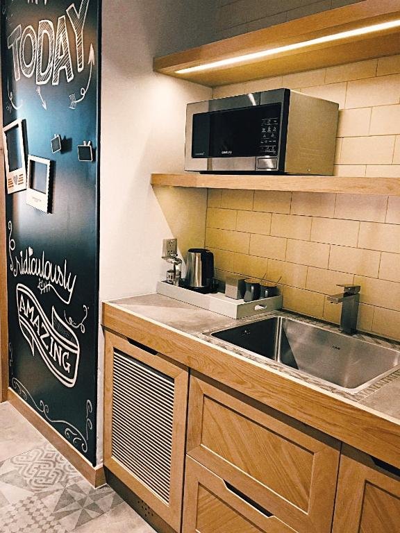 A kitchenette with a microwave on a lit wooden shelf, a steel sink, a kettle and tea things, and a chalkboard wall reading Today and Ridiculously Amazing