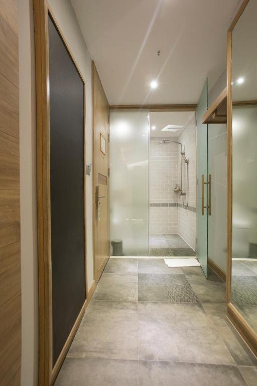 A stone-tiled hallway with a full-length mirror, the entry door, and frosted glass doors open onto a tiled rain shower