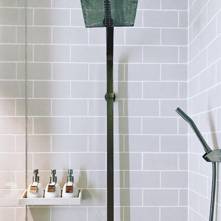 The rain shower column, a hand shower and three toiletry bottles with leather tags on a shelf against white tiles