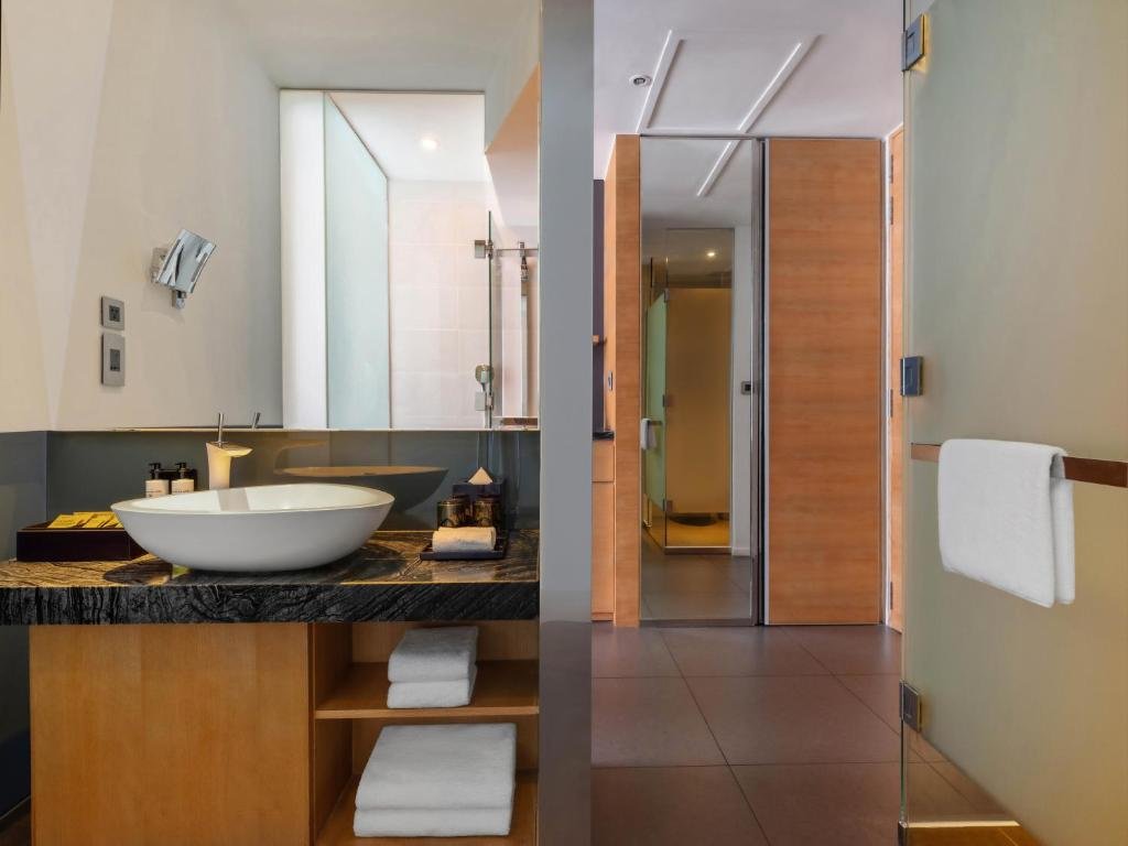 A bowl basin on a dark marble counter with folded towels on the shelves below, a mirror, and frosted glass doors to the shower and toilet
