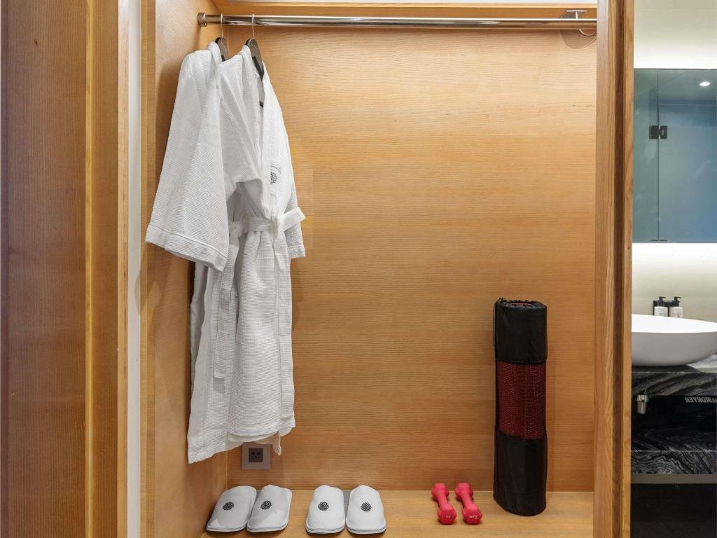 An oak wardrobe with two white bathrobes and slippers, a yoga mat and a pair of dumbbells, and the basin visible beyond