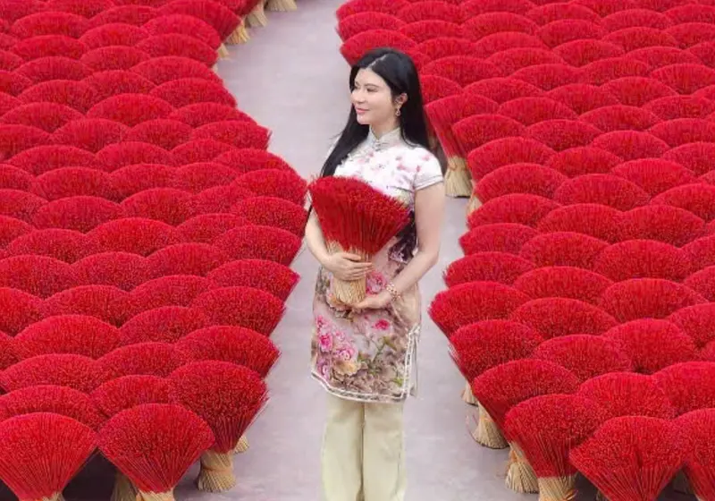 A woman and child in ao dai walking the narrow path between fans of red incense