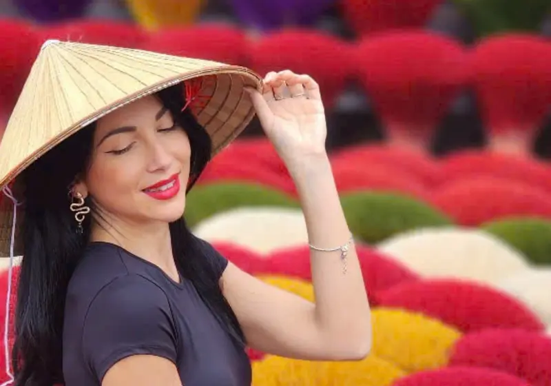 A visitor in a conical hat in front of red, yellow and green incense fans