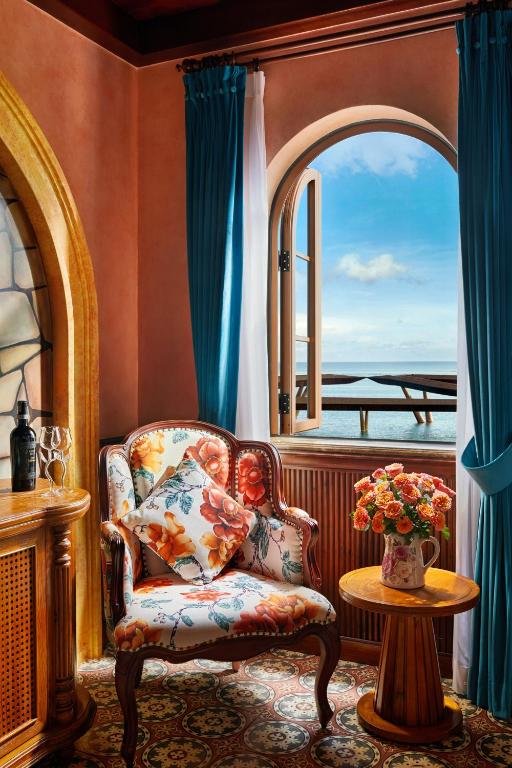 A floral armchair and a small round table with roses beside an arched window opened onto the sea and a footbridge over the water
