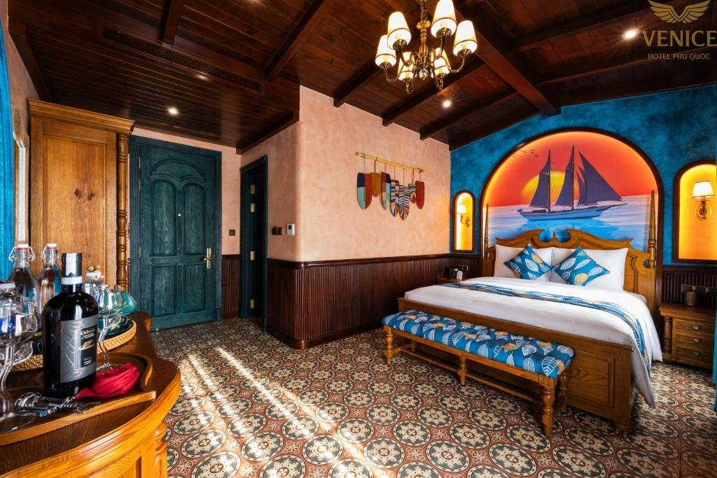 The room from the door end: the bed and bench beneath a sunset sailing-ship mural on a blue wall, lamp niches either side, and a drinks tray on the console in the foreground