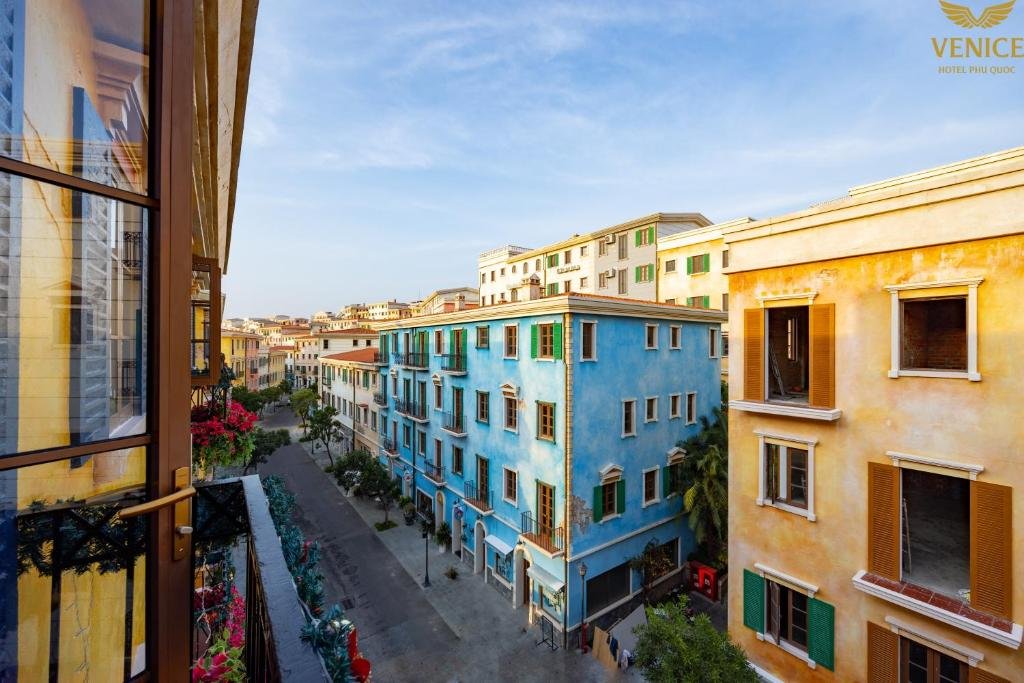 The view from the room: a street of pastel buildings in blue and yellow with green shutters, running away between palms and planters under a clear sky