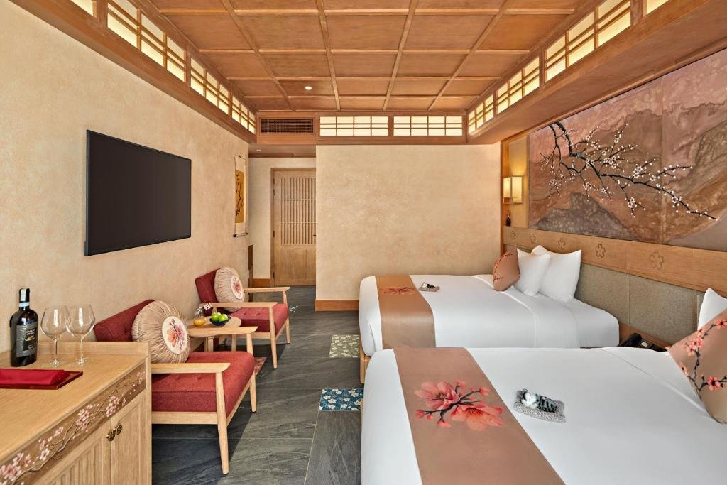 The same room from the window end: both beds along the mural wall, a wall-mounted TV opposite above a blossom-painted console, and two armchairs with a round table