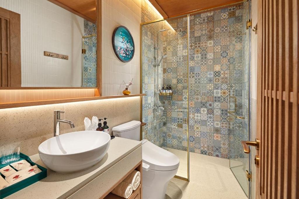 The vanity from the doorway: a vessel basin and mirror lit from beneath, the tiled walk-in shower behind a glass screen, and a slatted wooden door