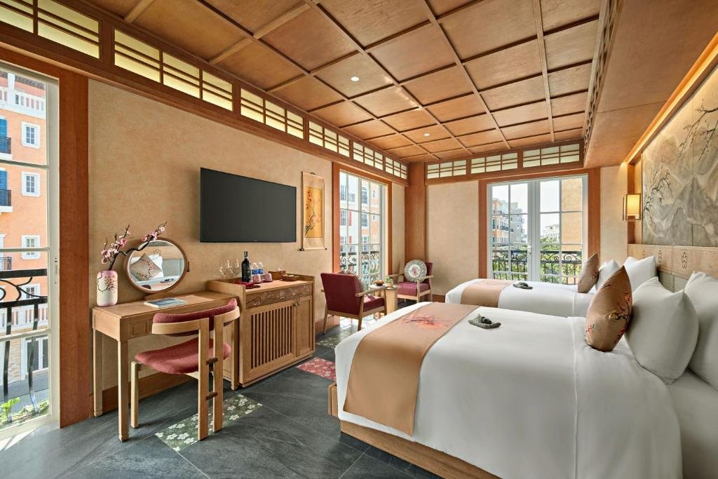 The corner of the room: balcony doors on two walls looking onto the pastel buildings of Sunset Town, a dressing table with a round mirror, a TV, and two armchairs by the window
