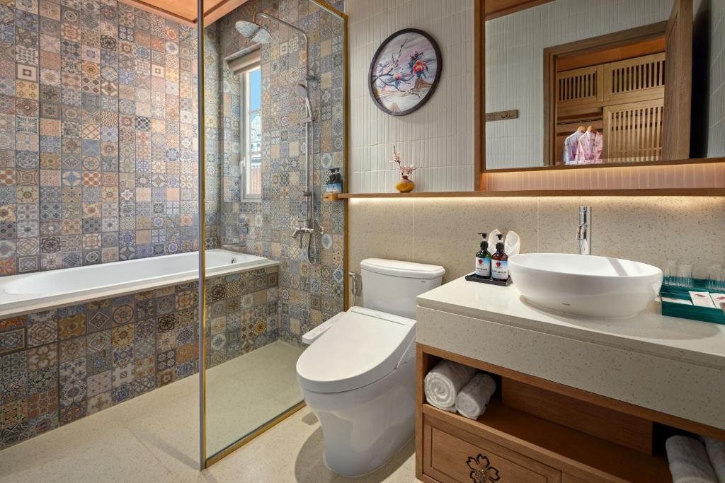 The bathroom: a built-in bathtub and a walk-in shower behind glass, both against a wall of patterned encaustic tile, with a toilet and a vessel basin on a terrazzo counter