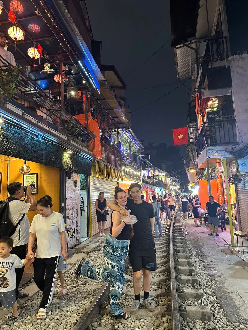 Lantern-lit cafes lining the narrow tracks of Hanoi Train Street, visitors standing beside the rails