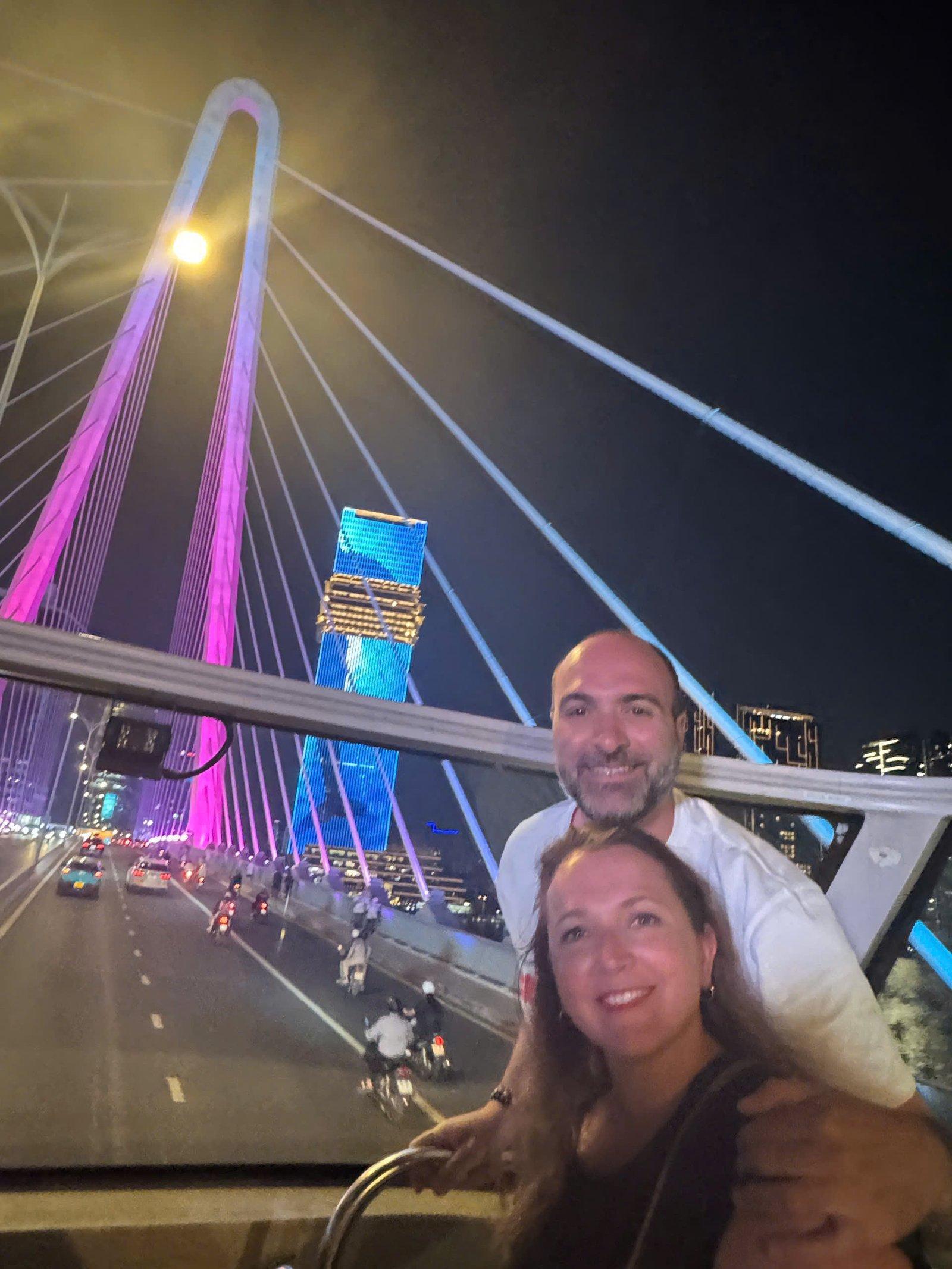Guests on the open top deck with a lit bridge and the city skyline behind them at night