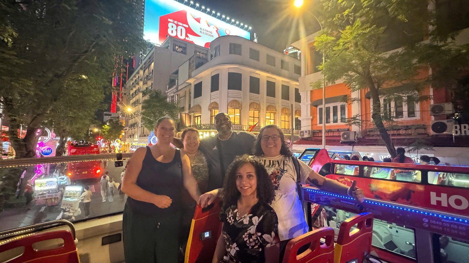 Guests on the open top deck at night on Dong Khoi, shopfronts lit up behind them