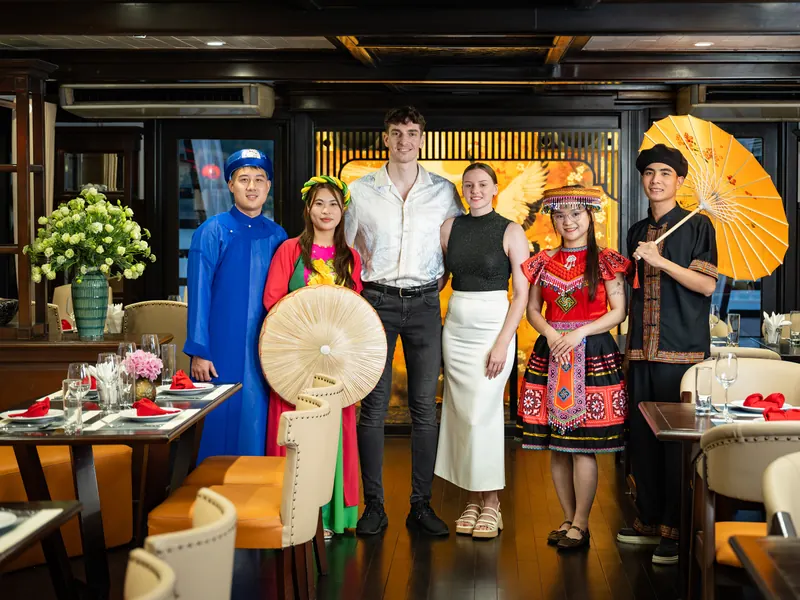 Guests posing for a souvenir photograph with crew members dressed in traditional Vietnamese costume