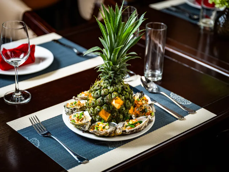 Grilled oysters served around a fresh pineapple on a plated table setting