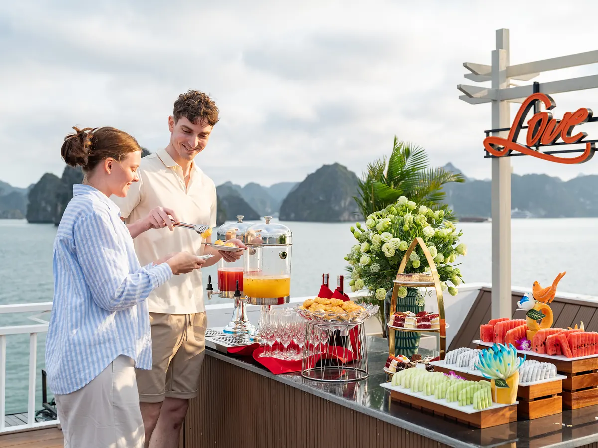 Guests serving themselves from a sunset party table of juices, pastries and canapes on the open deck with karsts behind