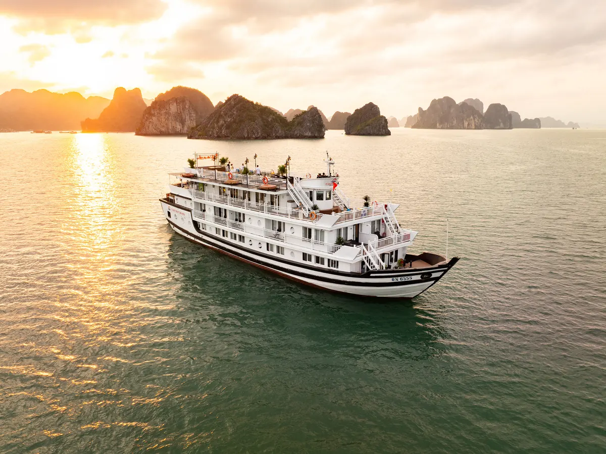 Cozy Grand seen from the water at sunrise, her three decks lit against the limestone islands of Halong Bay