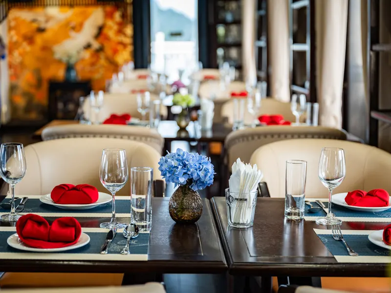 A laid dinner table with red folded napkins, wine glasses and a vase of blue hydrangeas