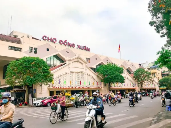 The pink facade of Cho Dong Xuan, Hanoi’s largest covered market, with cyclists and motorbikes passing in front