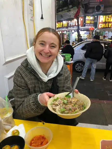 A traveller holding a bowl of pho at a street kitchen