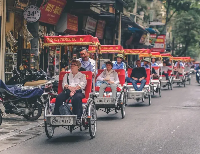 A convoy of cyclos carrying a small group in single file past Old Quarter shopfronts