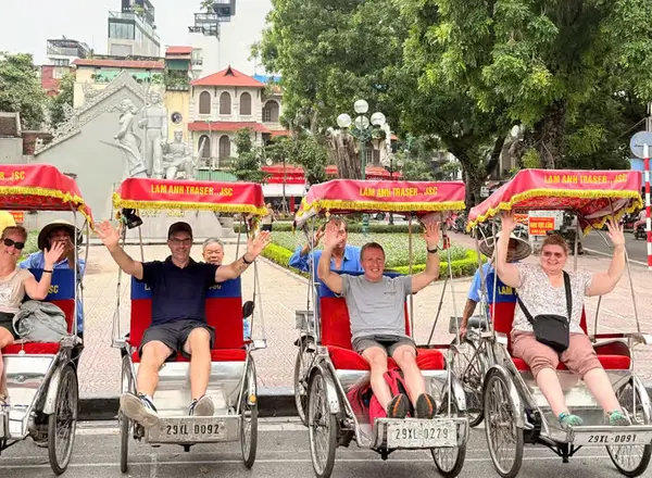 Four guests raise their arms from the seats of a row of parked cyclos