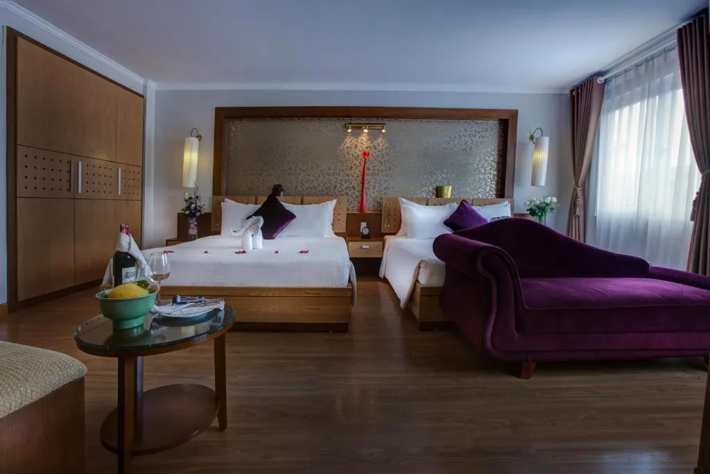 Room with two beds under a gold damask headboard panel and a purple chaise longue