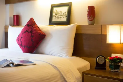 Superior Double: pillows and a red cushion against the wood headboard, with a clock and lamp on the bedside table