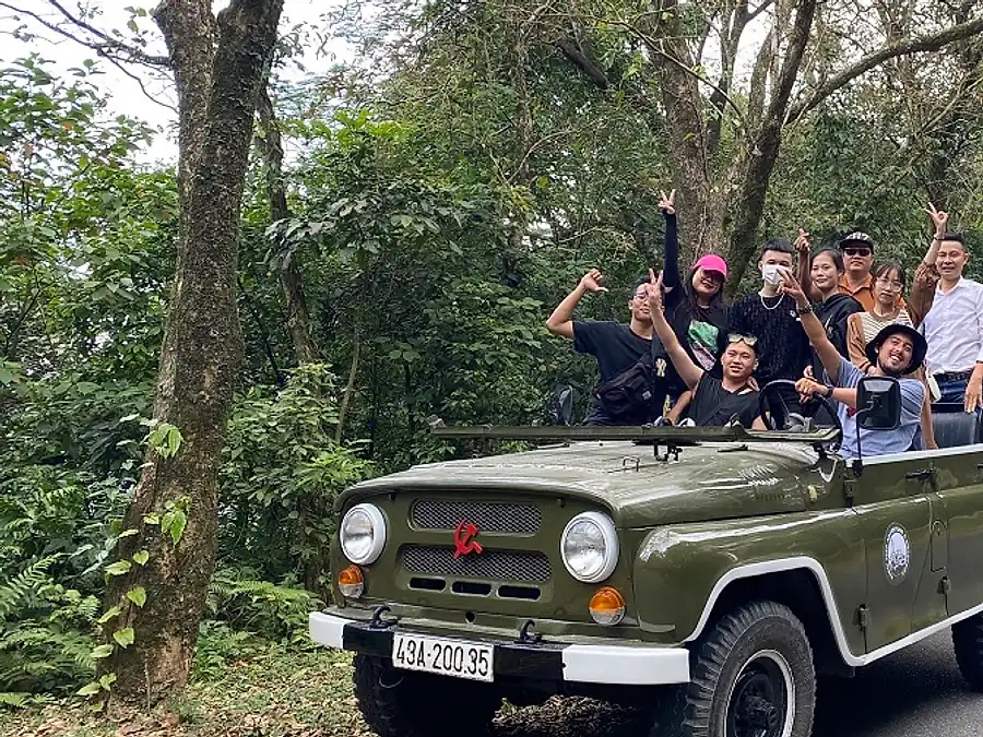 Guests riding in an open-top vintage army jeep on a country road in Ninh Binh