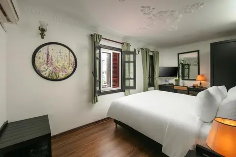Deluxe King: king bed below a moulded ceiling, with a shuttered window and desk