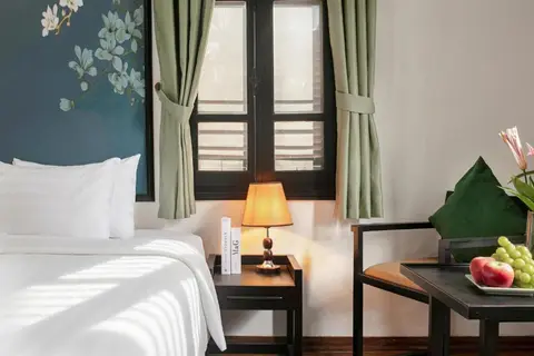 King Room with Balcony: bedside table and shuttered window beside the armchair