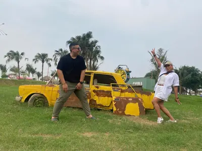 A rusted yellow vintage car set on the grass among palm trees as a photo prop